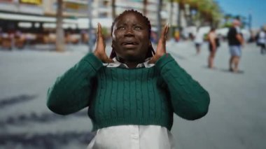 Yeşil kazaklı kadın yoğun bir sokakta duygularını ifade ediyor, şehir ve şehir manzarasıyla çevrili, dinamik açık hava enerjisi sergiliyor..