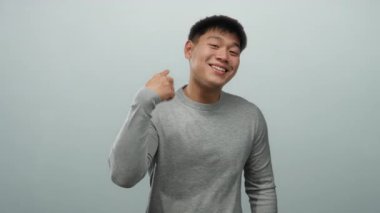 Gri süveter giyen genç Çinli adam izole edilmiş beyaz arka planda elleriyle jestler yapıyor, pozitiflikle gülümsüyor..