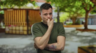 Şehir caddesinde düşünceli bir ifadeyle dolaşan genç adam ağaç gölgesinin altında dövmeleri ve günlük tarzını gösteriyor. Gündüzleri şehir yaşam tarzını çağrıştırıyor..