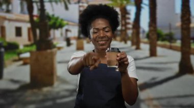 Önlüklü bir kadın, elinde kahve fincanı, elinde palmiye ağaçları, güpegündüz dışarı bakıyor..