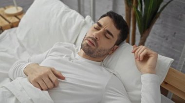 Beyaz çarşaflı, sıkıntılı ve kafası karışık görünen, modern bir evde yakalanmış, genç İspanyol bir adam yatak odasında bir kabustan uyandı..