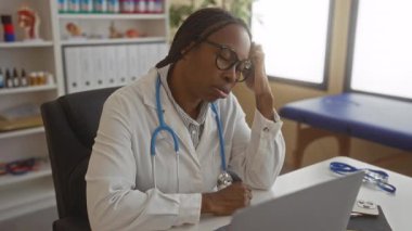 Masada dinlenen kadın doktor modern klinik çalışma ortamında steteskopla hastane ofisinde stresli görünüyor..