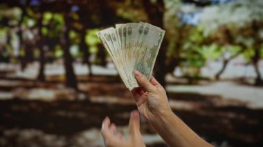 Yeşillik bir parkta dışarıdaki toprakları sayan bir adam, doğal bir şehir ortamında iş ya da finansal faaliyet gösteriyor..