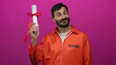 Turuncu hapishane tulumlu İspanyol adam pembe arka plana karşı diploma taşıyor. Eğitim ve reformu simgeliyor..