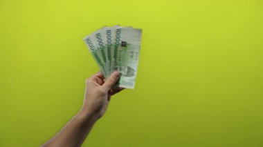 Güney Kore 'yi elinde tutan adam, zenginlik, finans ve para alışverişini vurgulayarak, eşsiz kültürel bağlam üzerine odaklanarak, canlı sarı bir arka plana karşı banknotlar kazandı..