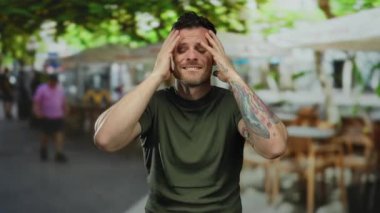 Dövmeli genç adam güneşli bir şehir terasında stresli görünüyor. Etrafı hareketli şehir hayatı ile çevrili. İç duygular ve canlı çevre arasındaki zıtlığı yakalıyor..