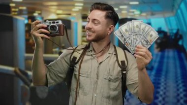 Spor salonunda gülümseyen ve fotoğrafçılıktan zevk alan kameralı genç bir adam Amerikan parası ve seyahat macerası sergiliyor..