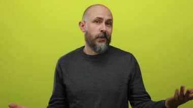 Sakallı, beyaz, kel bir adam. Sarı arka planda duruyor. Düşünceli ve anlamlı görünüyor..