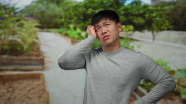 Parktaki genç adam gündüz vakti açık gökyüzünün altında yeşillik ve ağaçlarla çevrili gündelik kıyafetlerle düşünceli görünüyor..