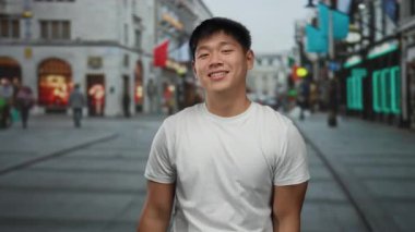 Genç Çinli bir adam gülümsüyor ve hareketli bir şehir caddesinde sokak ortasında el kol hareketi yapıyor..