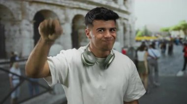 Beyaz gömlekli ve kulaklıklı genç adam Roma kolezyumunun yanında duruyor, Roma 'nın hareketli şehrinde sıradan bir açık hava havasını somutlaştırıyor..