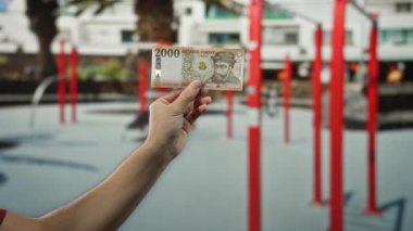 Macar forint banknotunu elinde tutan bir adam spor salonunda kırmızı ekipmanlarla çevrili..