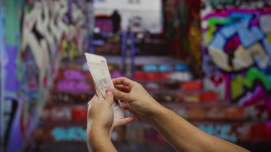 Canlı bir şehir graffiti arkaplanına karşı açık havada Türk lirası tutan adam, sokak işlerini ve finansal kavramları temsil ediyor..