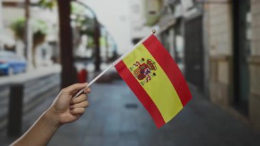 Arka planda bulanık bir sokak sahnesi olan, ulusal gurur ve kültürel kimlik teşhir eden bir açık hava kasabasında İspanyol bayrağını tutan bir el..