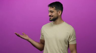 Çekici bir adam pembe arka plan üzerinde el hareketleriyle gülümsüyor ve bej gömlek giyiyor.