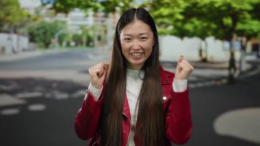 Şehir caddesinde gülümseyen kırmızı ceketli bir kadın güneşli bir günün tadını çıkarıyor açık havada canlı bir atmosfer yaratıyor.