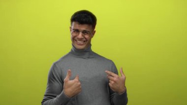 Gri balıkçı yakalı genç adam canlı sarı bir arka plana karşı gülerek neşe ve modern tarzını sergiliyor..