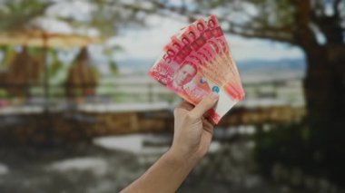 Bir park ortamında Filipinli pezosu tutan bir adam, beyaz erkek eli açık havada ağaçlar arasında doğal ışık altında ve bulanık arka planda vurguluyor..