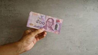 Tayland 'da somut arka planda Thai baht banknotunun el ele tutulması, para birimi özellikleri ve tasarım detayları sergilenmesi.