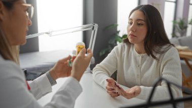 Kadın hasta, kadın doktoru dikkatlice dinliyor. Klinik ortamında ilaçları açıklıyor. Profesyonel bir sağlık hizmetleri ortamı sergiliyor..