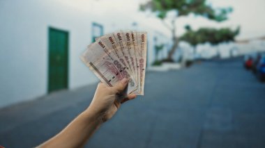 Bir şehir caddesinde Suudi Arabistan riyal banknotları tutan adam, açık bir şehir ortamında döviz değişimi sergiliyor..