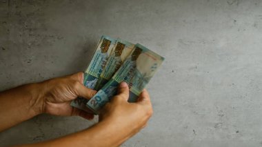 Beton duvar yüzeyine karşı birden fazla Hong Kong doları banknotları tutan eller, döviz kurunu veya para transferini vurguluyor.