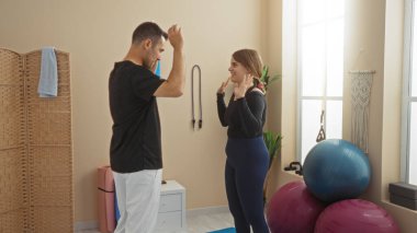 Spor salonunda gülümseyen erkek ve kadın spor aletleriyle dolu, neşeli bir bağlantı sergiliyor, motive edici bir ortamda zindelik ve kişisel gelişim gösteriyor..