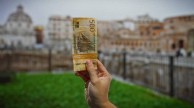 Roma kentsel caddesinde Norveç kronu tutan adam, şehir zemininde uluslararası finans ve yatırımı vurguluyor.