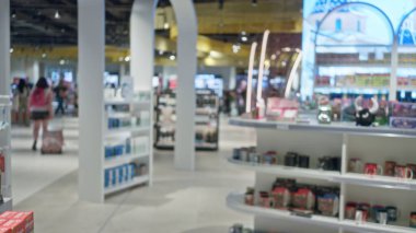 Alışveriş merkezinde raflar ve ürünlerle bulanık bir kadın, kalabalık alışveriş merkezi ortamında bokeh etkisi ile canlı bir iç atmosfer yaratıyor..