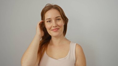 İzole edilmiş beyaz arka planda saçlarına dokunarak gülümseyen bir kadın doğal bir ifadeyle güzellik ve zarafet sergiliyor.