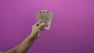 İzole edilmiş mor arka plan duvarı üzerinde Türk lirası banknotları tutan adam, para ve erkeklik odaklı canlı bir ortamda finansal konsept sergiliyor.