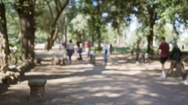 Güneşli bir günde bulanık ağaçlar, patikalar ve bokeh etkisi içeren Roma 'daki villa borghese bahçelerinde gezinen insanların odaksız sahnesi..