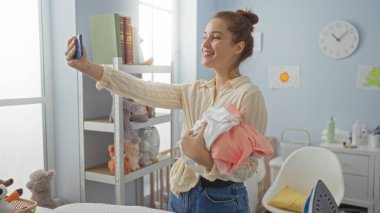 Çamaşır yıkarken gülümseyen ve parlak ev çamaşır odasında selfie çeken bir kadın. Pencereden içeri güneş ışığı giriyor..