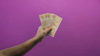 Elinde Türk lira banknotları tutan adam canlı mor arka plan duvarına karşı izole edilmiş..