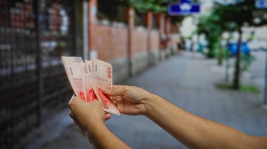 Kentsel bir sokakta elinde birkaç Tayvan doları tutan bir adam, şehirdeki yatırım, iş ve mali işlemlerin temaları vurgulanıyor.