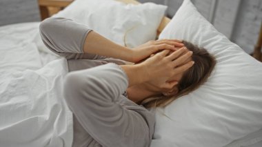 Kadın rahat bir yatak odasında dinleniyor, beyaz çarşaflarla rahat bir yatakta dinleniyor, günlük giysiler giyiyor, evde huzurlu bir sabah yakalıyor ve sakin bir ruh hali sergiliyor..