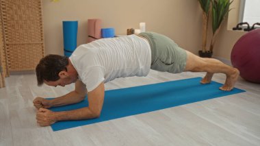 Olgun İspanyol adam, sağlık odasındaki yoga minderinde bitki ve mumlarla egzersiz yapıyor, fitness ve rahatlama için tahta poz veriyor..