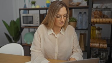 Ofis ortamında çalışan bir kadın, iç mekanlar ve raflarla çevrili, bir dizüstü bilgisayara odaklanmış, modern bir iş ortamını resmediyor..