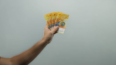 İzole edilmiş beyaz arka planda İsviçre frangı banknotları gösteren adam berraklığı ve finansal refahı vurguluyor..