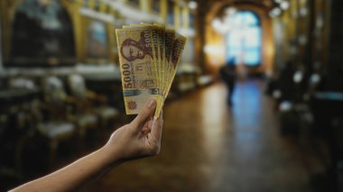 Bir müze odasında elinde Macar banknotları olan bir adam, tarihi bir ortamda para birimi temsili yoluyla kültür ve finansmanı sergiliyor..