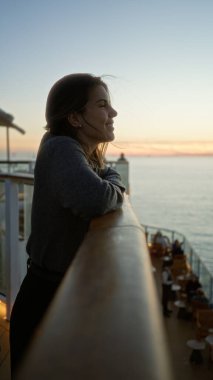 Bir yolcu gemisinin güvertesinde gün batımının tadını çıkaran bir kadın, dingin bir okyanus zeminiyle rahatlamış ve gülümsüyor genç güzelliğin ve hayat dolu seyahatin keşfi için..