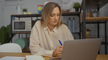 İç dekorasyonla çevrili bir dizüstü bilgisayarla masa başında çalışan genç bir kadın..