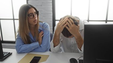 Gözlüklü bir kadın, modern ofis içlerindeki stresli adamla konuşuyor. İşyeri dinamiklerini gösteriyor ve zor bir iş gününde çalışanlar arasında duygusal destek veriyor..