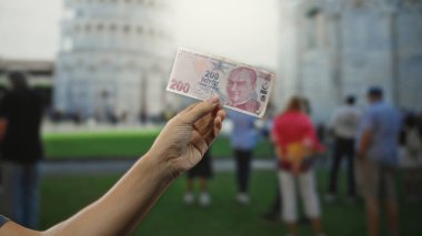 Elinde Türk lira banknotları tutan bir adam İtalya 'da sidik kulesine yaslanmış, kültürel değişim sergiliyor ve canlı bir şehir manzarasında seyahat ediyor..