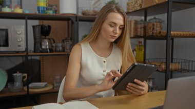 Ofiste tablet kullanan bir kadın, modern iç mekanla çevrili, sarışın bir yetişkinin profesyonel bir iç mekan içinde dijital çalışmalara dahil olduğu yerde..