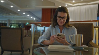 Lüks bir barda, akıllı telefon kullanan, zarif ama rahat bir ortamda kahvesini yudumlayan, modern yaşam tarzı ve sofistike bir ortam yakalayan bir kadın..