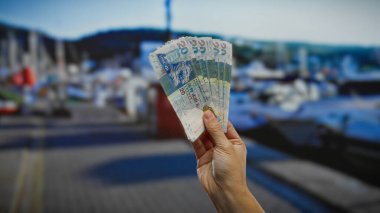 Hong Kong Doları banknotlarıyla el ele tutuşarak deniz kenarındaki bir ortamda yatırım ve para değişimi tasvir eden tekneler ve şehir manzarasıyla..