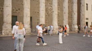Roma 'da bir kaldırım taşı caddesinde yürüyen insanlar, arka planda tarihi sütunlarla, dinamik kentsel çevreyi vurgulayan bulanık bir efektle yakalandılar..