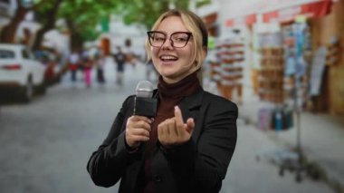Mikrofonlu kadın muhabir şehir piyasasının hareketli ortamında jest yapıyor.