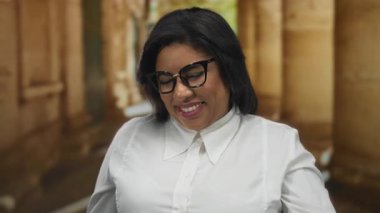 Genç, iri yarı Latin bir kadın, eski bir üniversitede kendinden emin bir şekilde gülümsüyor. Şık gözlükleri, tarihi mimariye karşı canlı kişiliğini ön plana çıkarıyor..